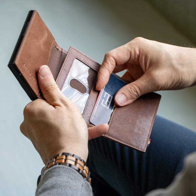 Person holding a brown leather wallet with a card inside on a light gray background