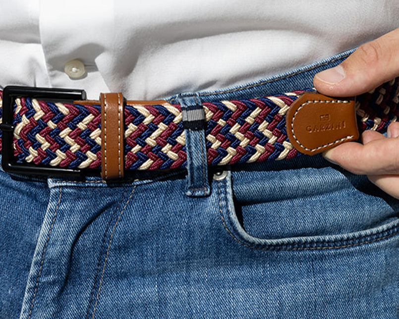 Person wearing a woven belt with a leather buckle, adjusting it on jeans.