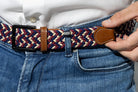 Person wearing a woven belt with a leather buckle, adjusting it on jeans.