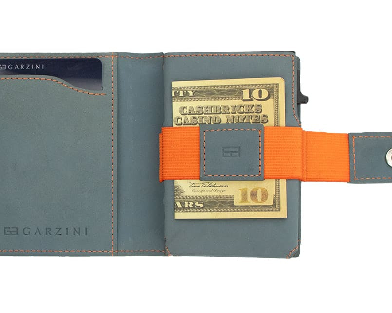Open Garzini Metal Wallet in blue leather with orange strap, holding a stack of cash secured by the strap
