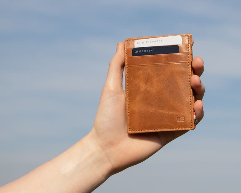 A hand holding the Essenziale Magic Wallet Brushed in Brushed Cognac with 2 cards in the card slot.