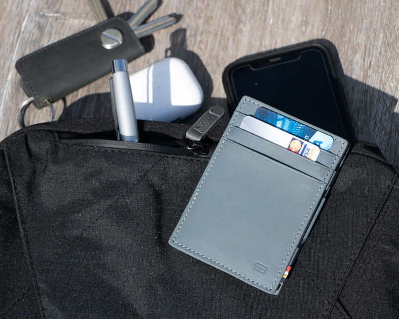 Essenziale Magic Wallet Vintage in Sapphire Blue partially placed inside a bag, accompanied by a pen, AirPods, Garzini Key Holder, and a phone in the background.