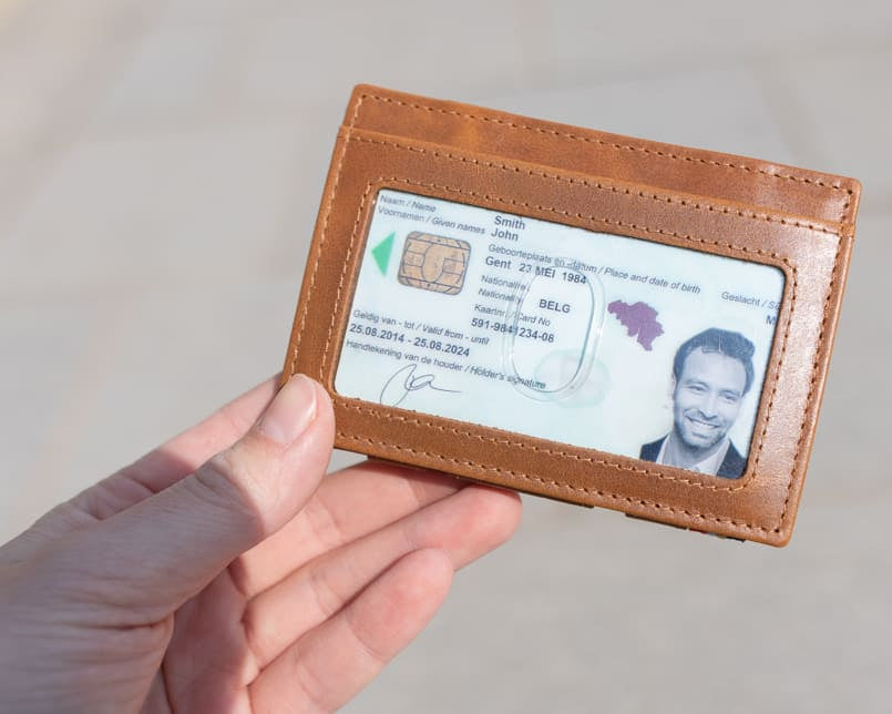 A hand showcasing the Brushed Cognac Essenziale Magic Wallet with an ID Window. The hand holds a card inserted into the ID window of the wallet.