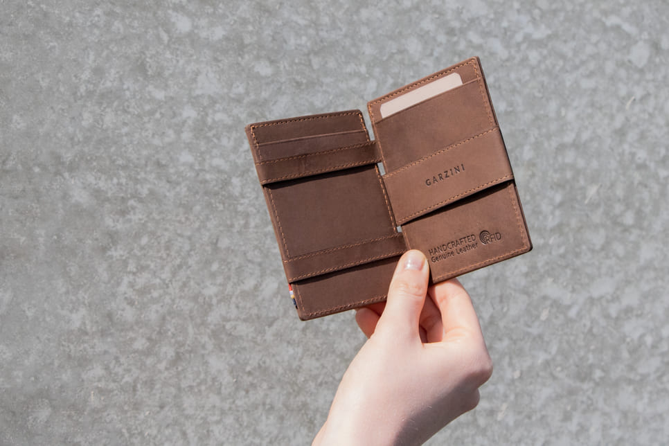 Open Cavare Magic Wallet Vintage in Java Brown with a money straps with a hand holding the wallet open.