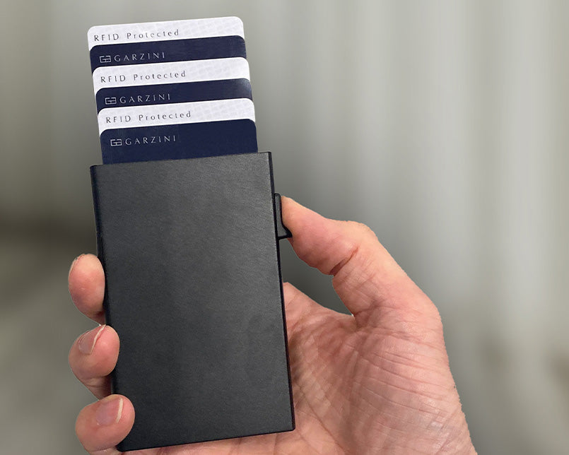 Hand holding a black Garzini metal wallet card holder with partially exposed cards