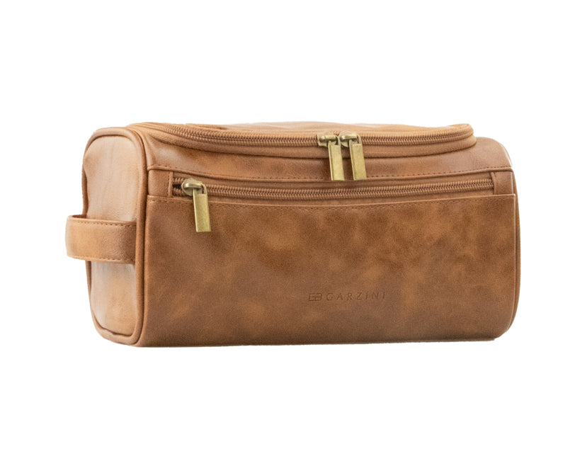 Cognac Garzini Toiletry Bag angled front side view, featuring sleek design and accessible zipper for easy travel use.