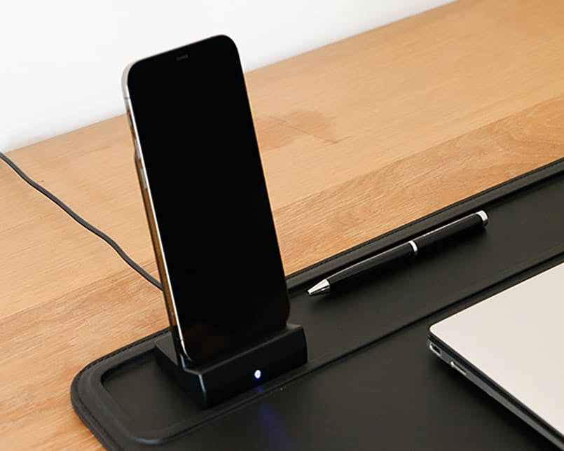 A wireless charger with a phone charging and a pen next to it.