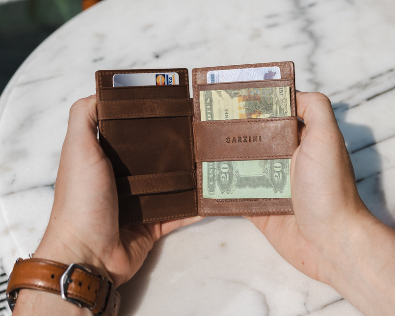 Two hands holdiing the Essenziale Magic AirTag Wallet in Brushed Brown open, inside cash and cards.