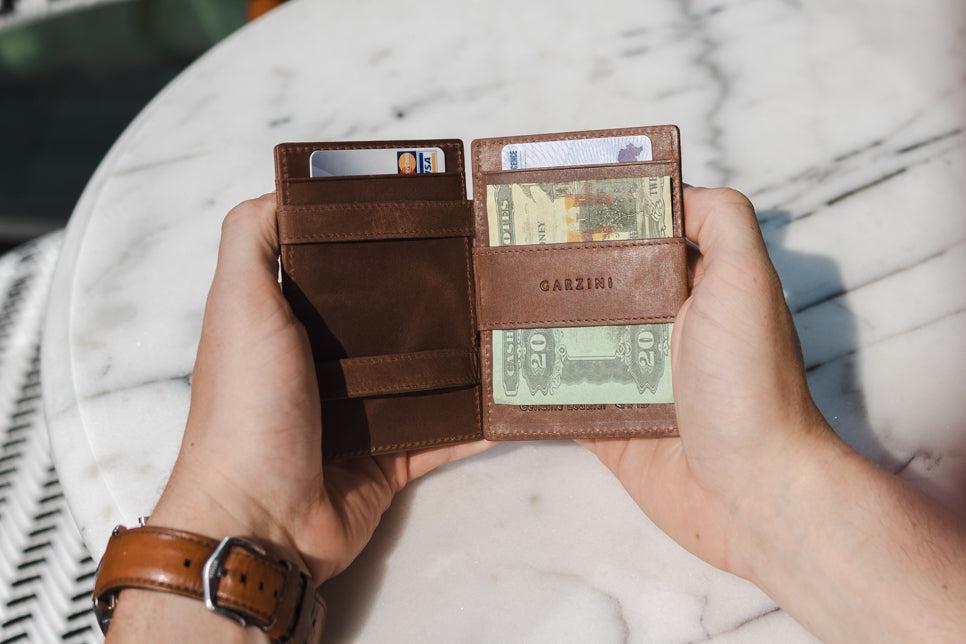 Two hands holdiing the Essenziale Magic AirTag Wallet in Brushed Brown open, inside cash and cards.