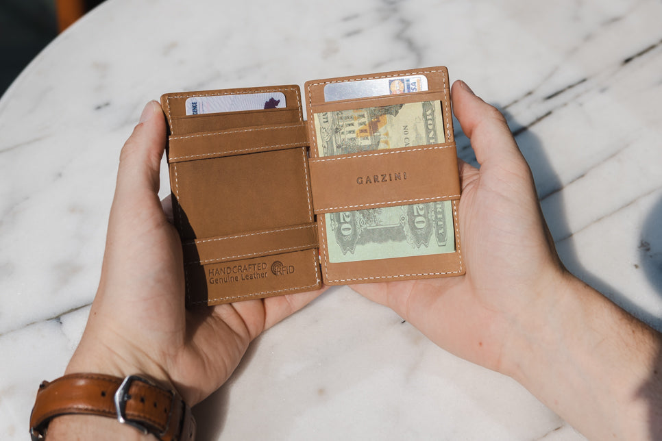 Two hands holdiing the Essenziale Magic AirTag Wallet in Brushed Cognac open, inside cash and cards.