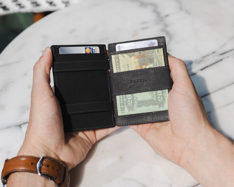 Two hands holding the Essenziale Magic AirTag Wallet in Carbon Black open, inside cash and cards.