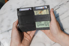 Two hands holdiing the Essenziale Magic AirTag Wallet in Brushed Black open, inside cash and cards.