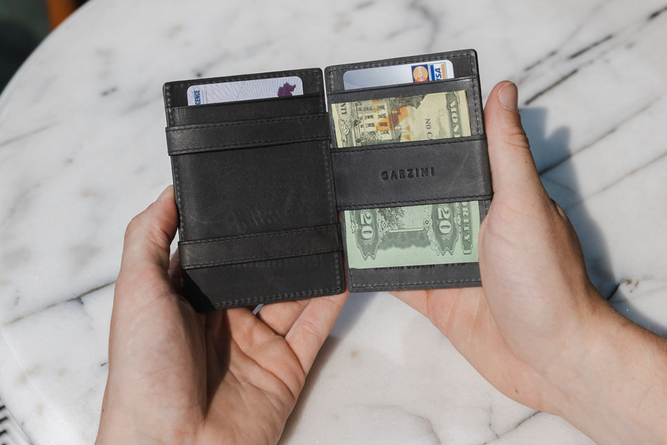 Two hands holdiing the Essenziale Magic AirTag Wallet in Brushed Black open, inside cash and cards.