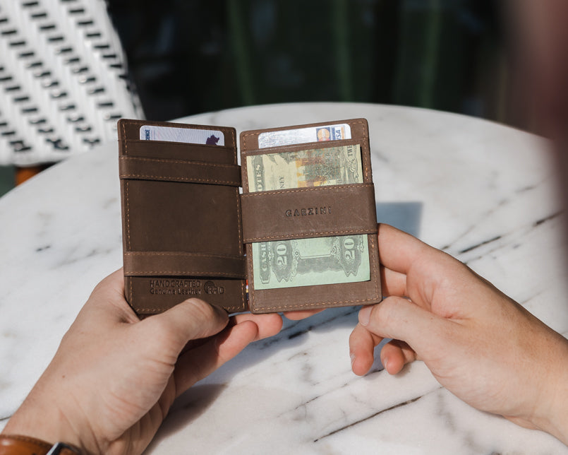 Two hands holding the Essenziale Magic AirTag Wallet in Java Brown open, inside cash and cards.