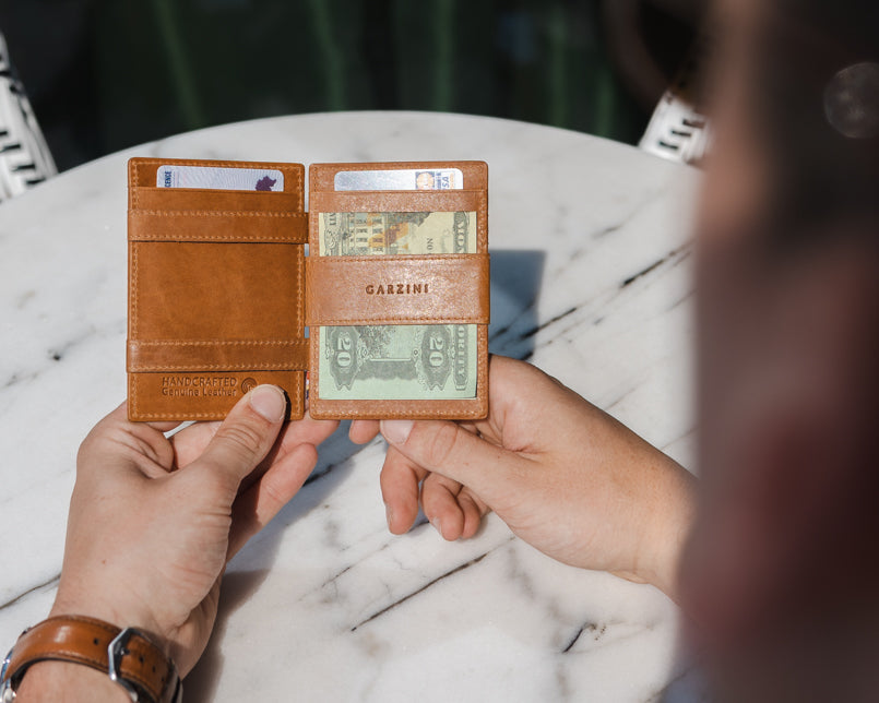 Two hands holdiing the Essenziale Magic AirTag Wallet in Brushed Cognac open, inside cash and cards.