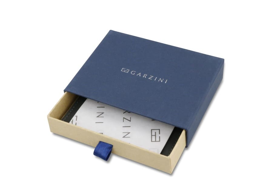 Half-open blue box with Garzini brand name. Inside the box, the Camel Brown wallet is wrapped in tissue paper, placed in a light cardboard box with a blue strap.