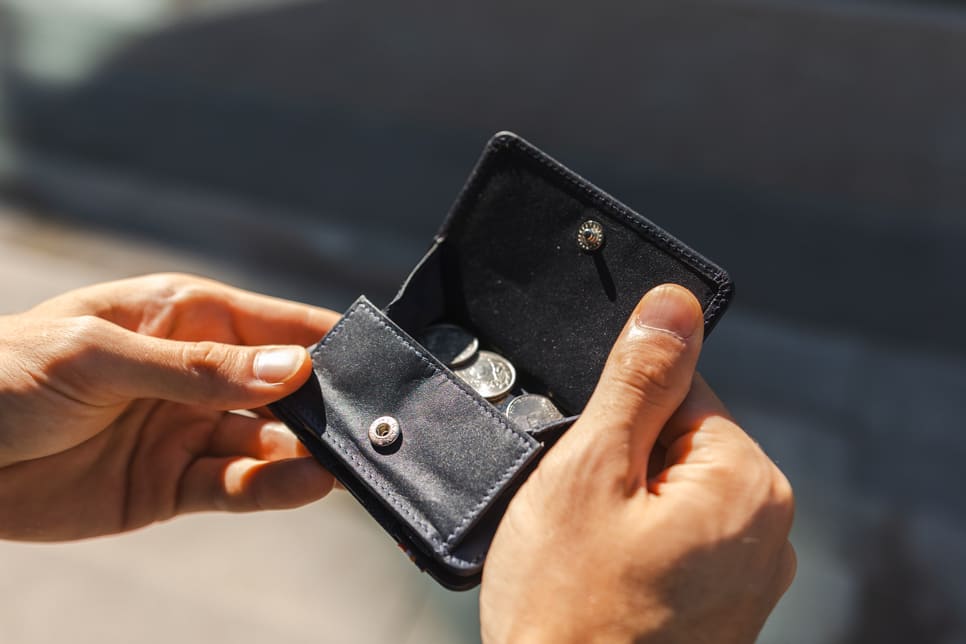 A hand holding the wallet with the coin pocket open and money inside.