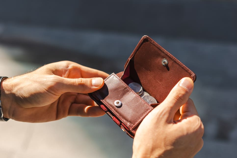 A hand holding the wallet with the coin pocket open and money inside.