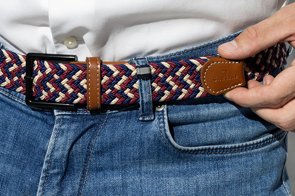 Person wearing a woven belt with a leather buckle, adjusting it on jeans.