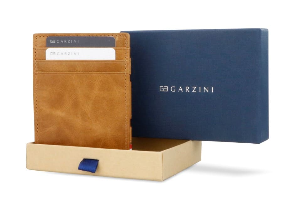 Half-open blue box with Garzini brand name Inside the box, the Brushed Cognac Wallet Brushed is wrapped in tissue paper, placed in a light cardboard box with a blue strap.