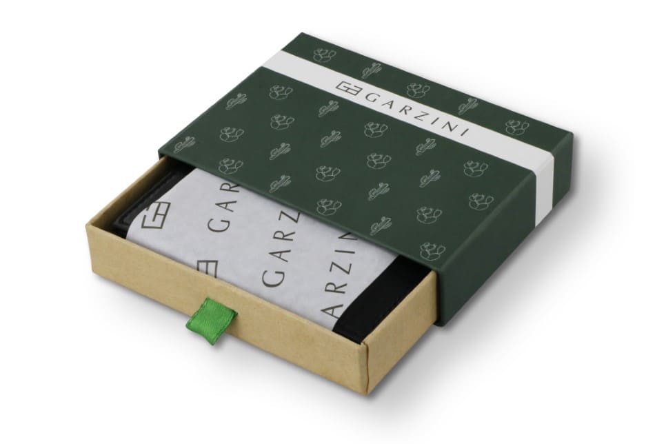 Half-open green box with Garzini brand name, featuring cactus icons. Inside the box, the Vegan Cactus Black wallet is wrapped in tissue paper, placed in a light cardboard box with a green strap.