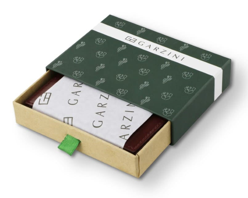 Half-open green box with Garzini brand name, featuring cactus icons. Inside the box, the Vegan Cactus Burgundy wallet is wrapped in tissue paper, placed in a light cardboard box with a green strap.