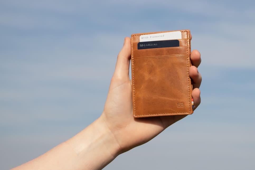 A hand holding the Essenziale Magic Wallet Brushed in Brushed Cognac with 2 cards in the card slot.