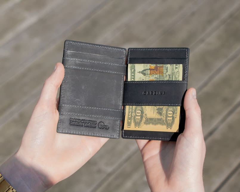 2 hands holding the Essenziale Magic Wallet Vintage in Carbon Black with money on one side open.