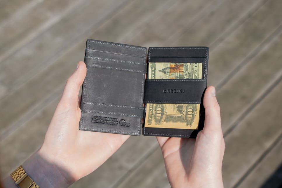2 hands holding the Essenziale Magic Wallet Vintage in Carbon Black with money on one side open.