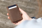 Essenziale Magic Wallet Vintage in Java Brown partially placed inside a bag, alongside a pen, AirPods, and a phone in the background.