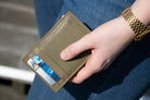 A hand holding the Essenziale Magic Wallet Vintage in Olive Green with 2 cards in the card slot. 