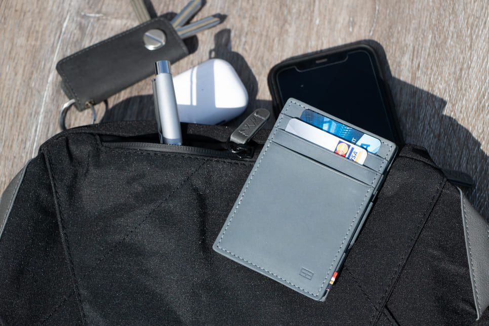 Essenziale Magic Wallet Vintage in Sapphire Blue partially placed inside a bag, accompanied by a pen, AirPods, Garzini Key Holder, and a phone in the background.