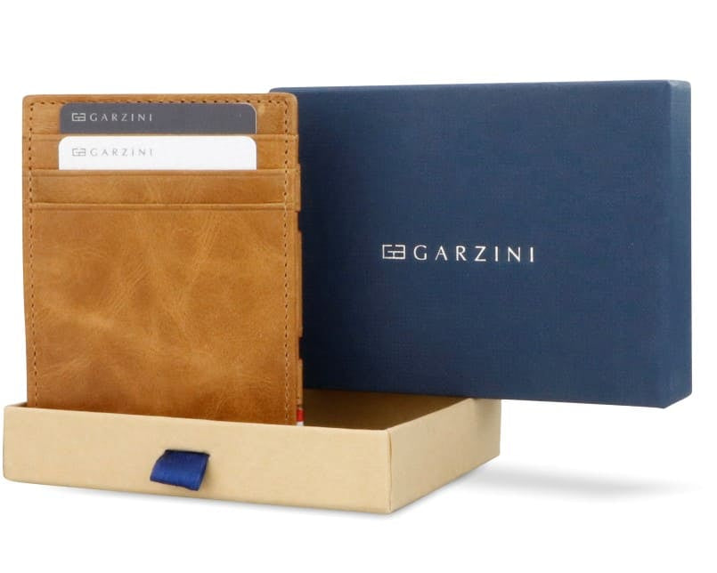 Half-open blue box with Garzini brand name. Inside the box, the Cognac wallet is wrapped in tissue paper, placed in a light cardboard box with a blue strap