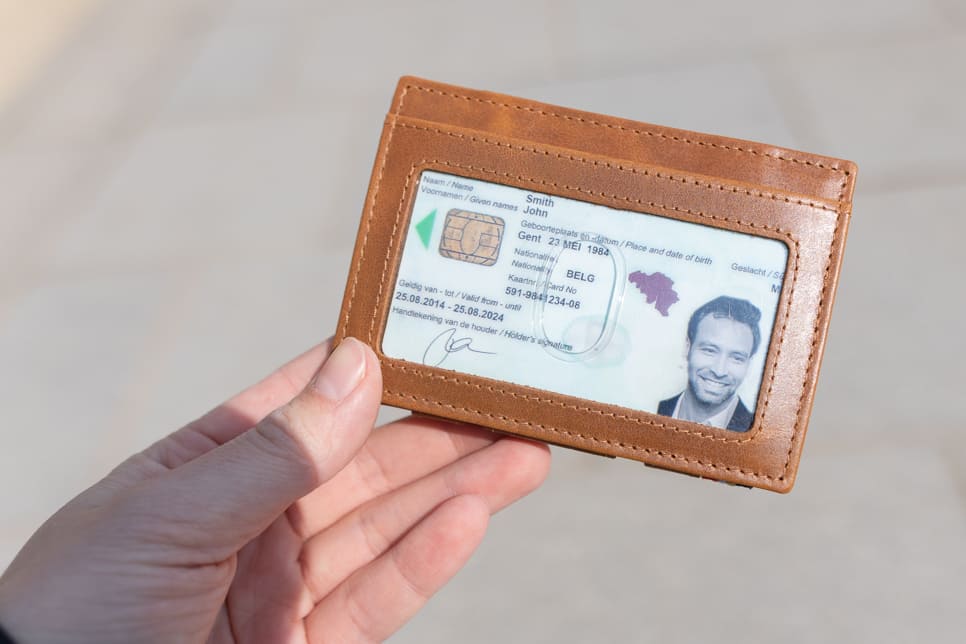 A hand showcasing the Brushed Cognac Essenziale Magic Wallet with an ID Window. The hand holds a card inserted into the ID window of the wallet.