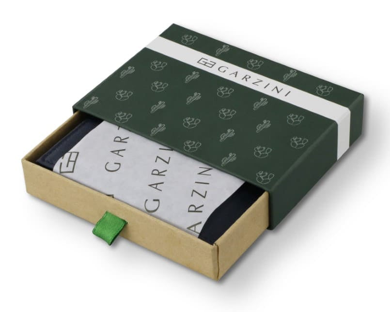 Half-open green box with Garzini brand name, featuring cactus icons. Inside the box, the cactus Blue wallet is wrapped in tissue paper, placed in a light cardboard box with a green strap.