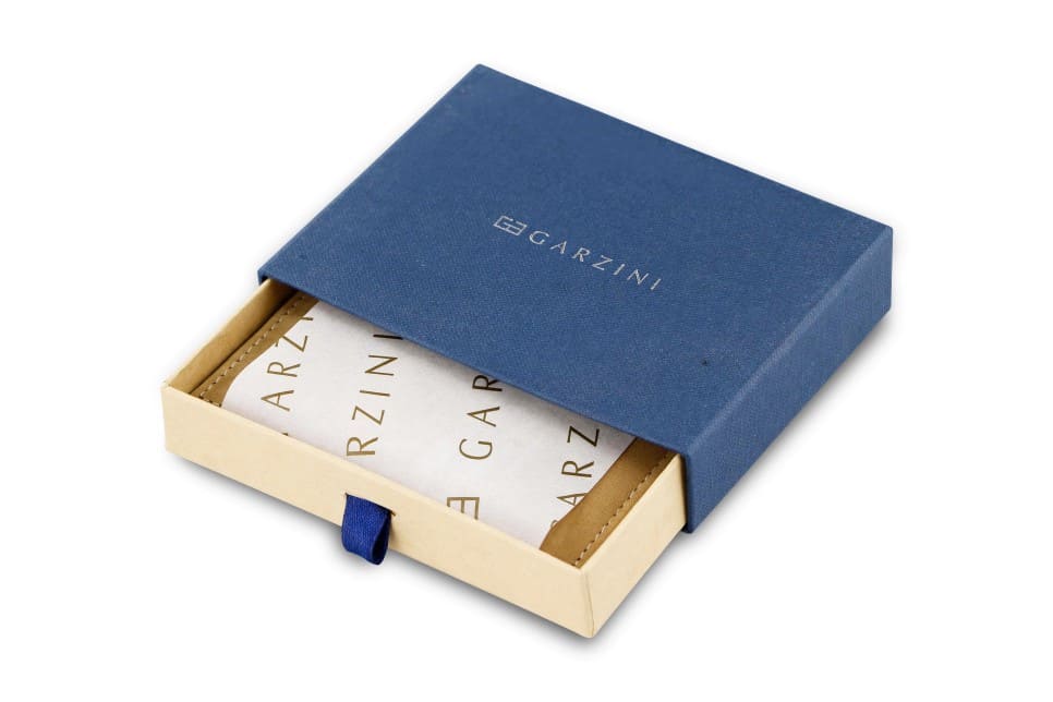 Half-open blue box with Garzini brand name. Inside the box, the Camel Brown wallet is wrapped in tissue paper, placed in a light cardboard box with a blue strap