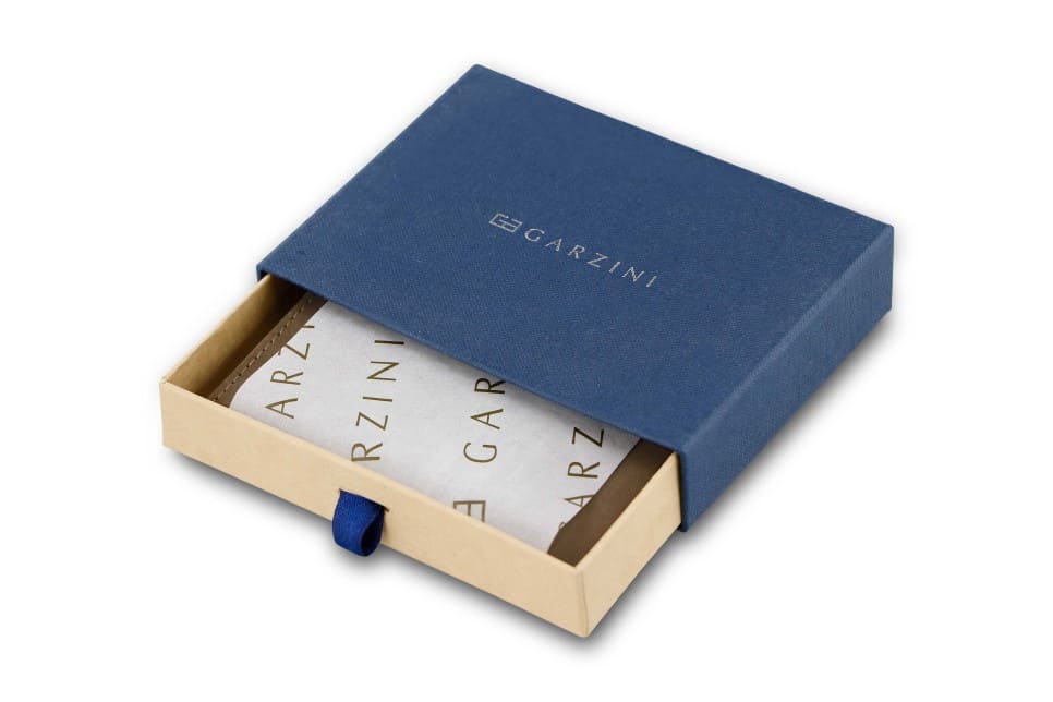 Half-open blue box with Garzini brand name. Inside the box, the Java Brown wallet is wrapped in tissue paper, placed in a light cardboard box with a blue strap