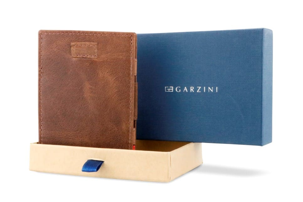 Half-open blue box with Garzini brand name Inside the box, the Brushed Brown wallet is wrapped in tissue paper, placed in a light cardboard box with a blue strap.