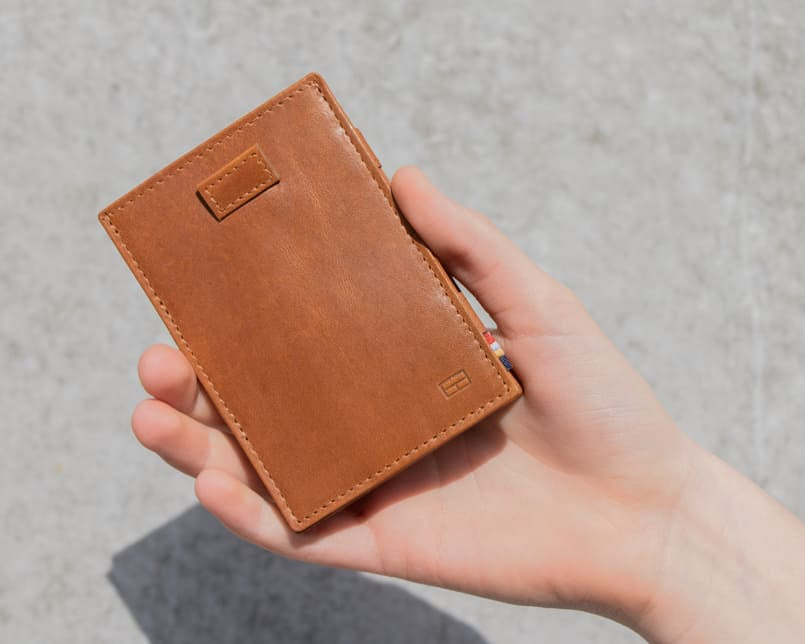 "Outside image of the front view of Cavare Magic Wallet Brushed in Brushed Cognac with a hand holding it open. "