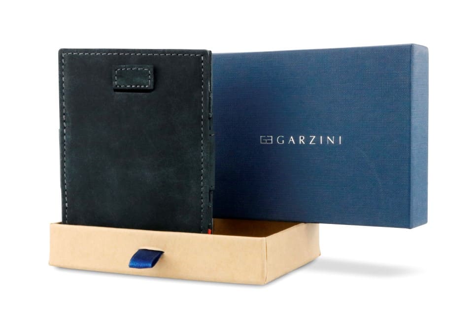 Half-open blue box with Garzini brand name Inside the box, the Carbon Black wallet is wrapped in tissue paper, placed in a light cardboard box with a blue strap.