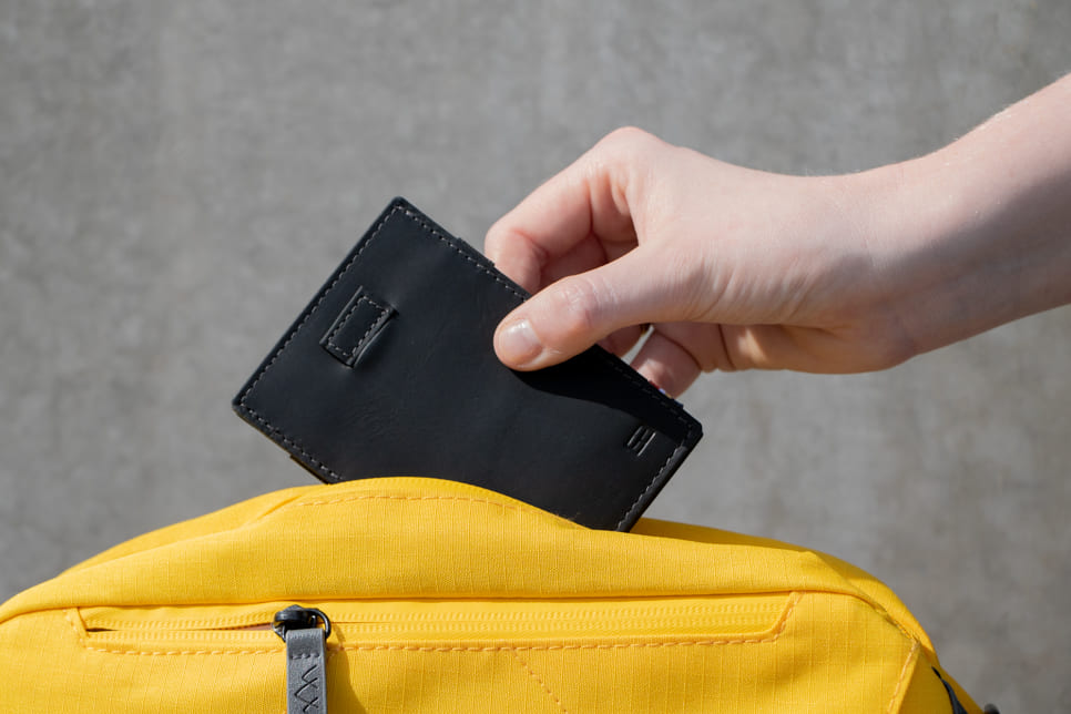 A Cavare Magic Wallet Card Sleeve Vintage Carbon Black hold by a hand put into a bag.