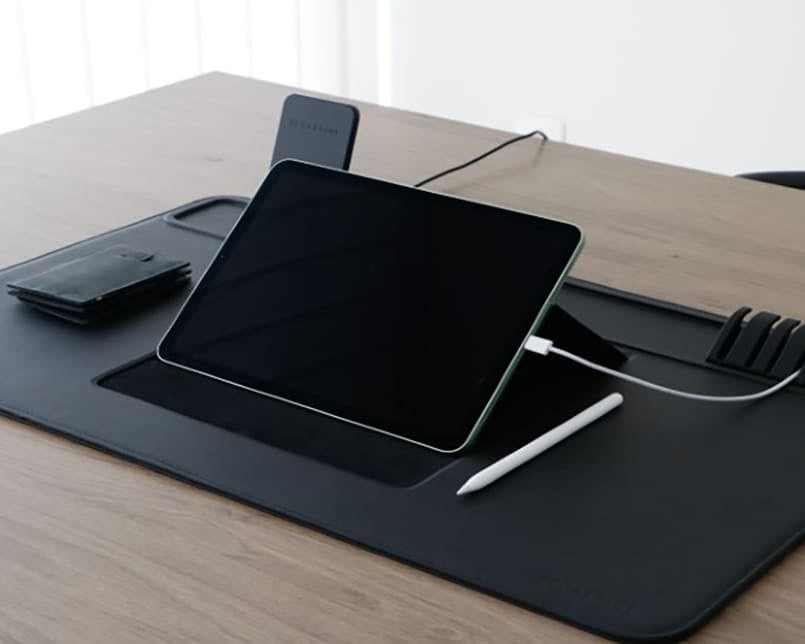 lifestyle image of the desk mat set up with ipad, cable holder, wireless charger, wallet and pen