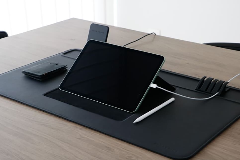 lifestyle image of the desk mat set up with ipad, cable holder, wireless charger, wallet and pen