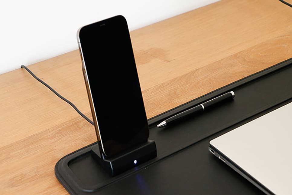 A wireless charger with a phone charging and a pen next to it.
