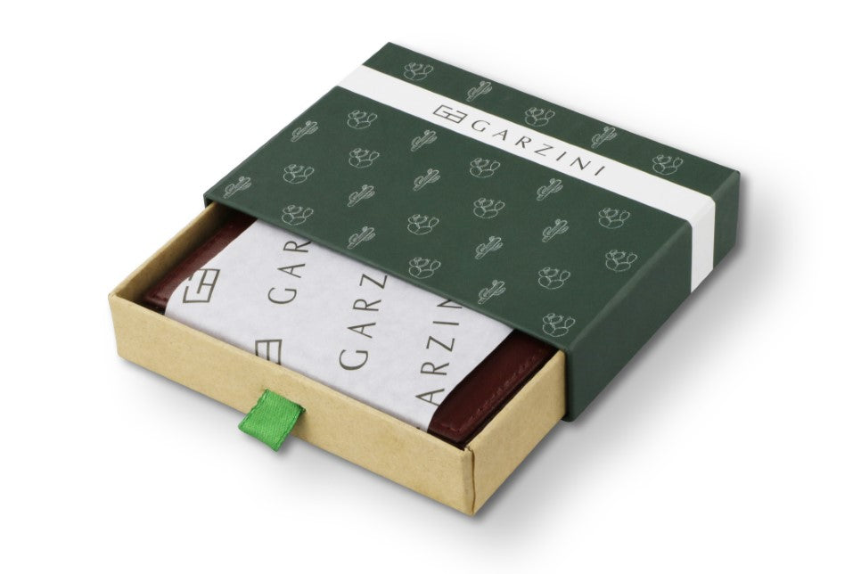 Half-open Burgundy box with Garzini brand name, featuring cactus icons. Inside the box, the Cactus Burgundy wallet is wrapped in tissue paper, placed in a light cardboard box with a Burgundy strap.